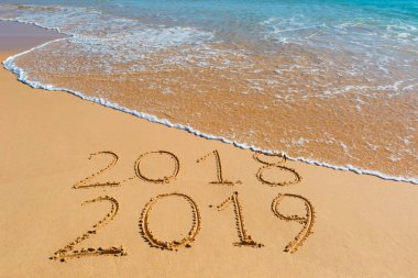 2018 2019 inscription written in the wet yellow beach sand being washed with ocean water wave. Concept of celebrating the New Year at some exotic place. clipart
