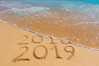 2018 2019 inscription written in the wet yellow beach sand being washed with ocean water wave. Concept of celebrating the New Year at some exotic place. clipart