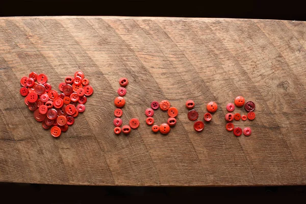 the word love made with red sewing buttons on wood