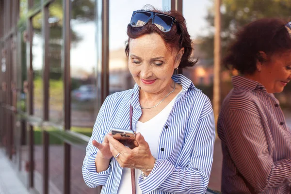 mature attractive stylish woman retired using mobile phone app for smartphone outdoors on summer day