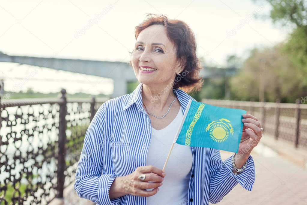 Portrait of a mature attractive stylish woman retired with a flag of Kazakhstan on a street in a summer sunny day. Welcome to Kazakhstan
