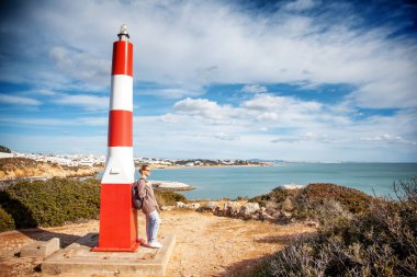 Bir kız gezgin deniz feneri bir tepenin üstüne tarafından standları ve okyanus, Algarve, Portekiz, popüler bir hedef için seyahat Avrupa'da bakar