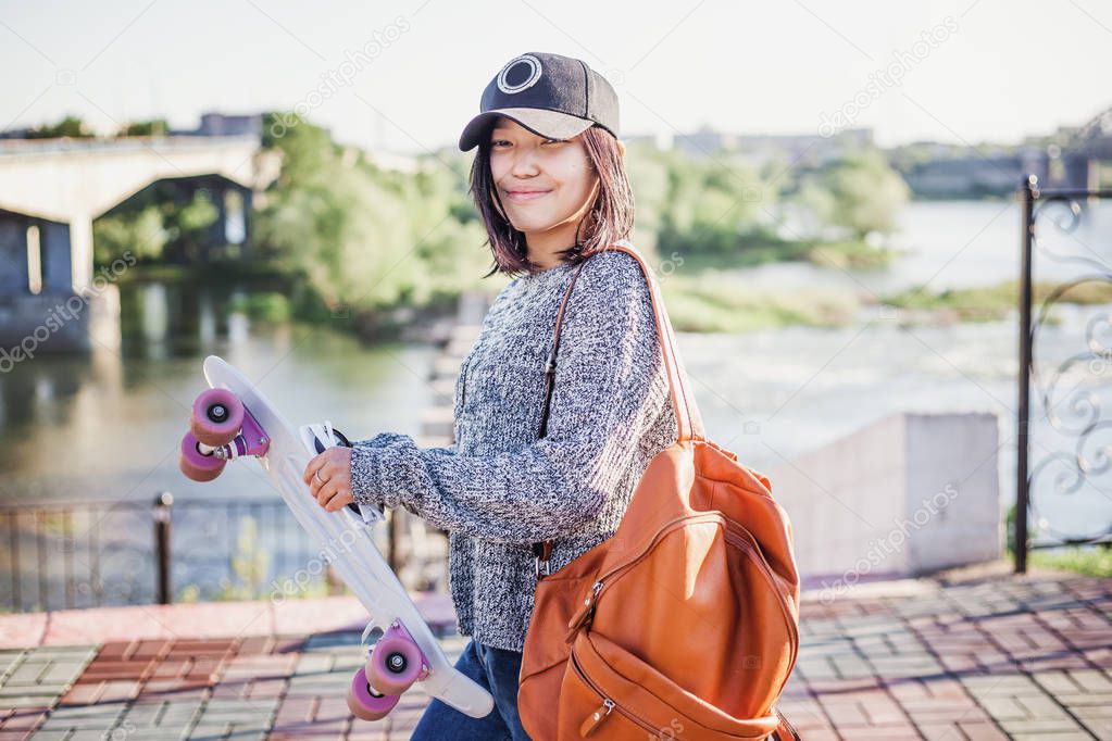 cute attractive stylish asian girl teenager 15-16 years old on city streets with skateboard in hands, millenial, youth lifestyle