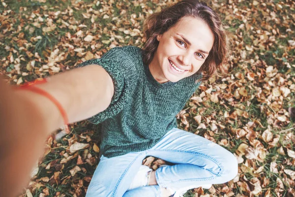 Красивая Молодая Женщина Сидит Парке Осенней Листве Делает Селфи Смартфоне — стоковое фото