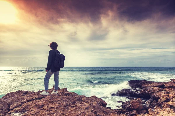 Genç kadın gezgin bir sırt çantası ile standları, deniz kıyısı ve parlak renkli günbatımı bakmak, retro tonlama ile bir resim