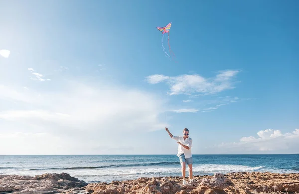 Young woman in a white shirt and shorts launches a kite on the seashore, travel and vacation concept, the joy of life