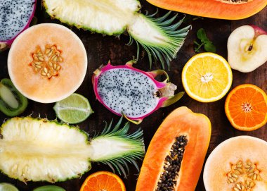 Bir ahşap masa, papaya, dragon meyve, kavun, portakal, greiprut, kivi, limon, ananas üzerinde farklı tropikal meyve. Üstten görünüm