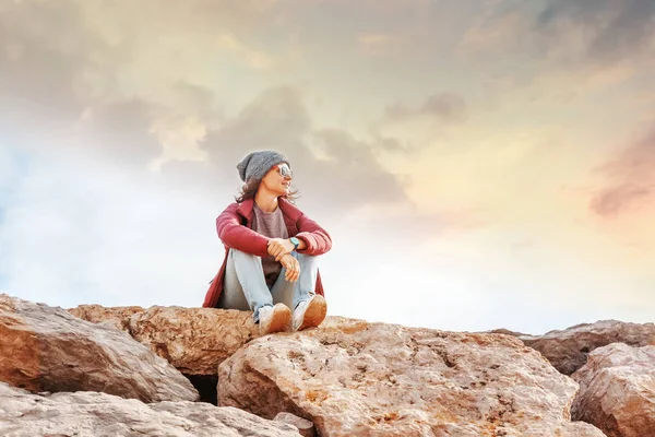 美丽的年轻女子旅行者坐在岩石上对蓝天在帽子和太阳镜阿尔加维 葡萄牙 — 图库照片