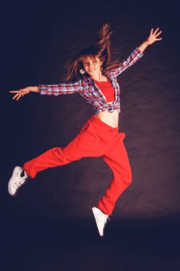 Genç güzel kadın kız kırmızı pantolon ve ekose gömlek karşı karanlık bir arka plan atlama içinde hip hop dans