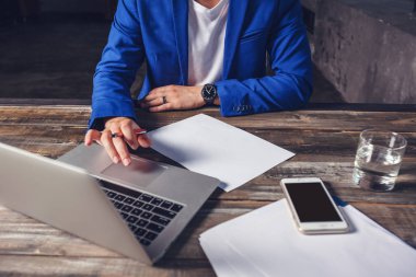 Eller üst, bir dizüstü bilgisayar, yaprak kağıt, bir telefon, bir bardak su ahşap bir masa üzerinde bir saat içinde mavi elbiseli bir işadamı. İş kavramı