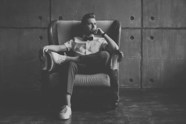 Genç çekici ciddi göz alıcı erkek hipster beyaz gömlek ve gri arka plan üzerinde sandalyede oturan kelebek