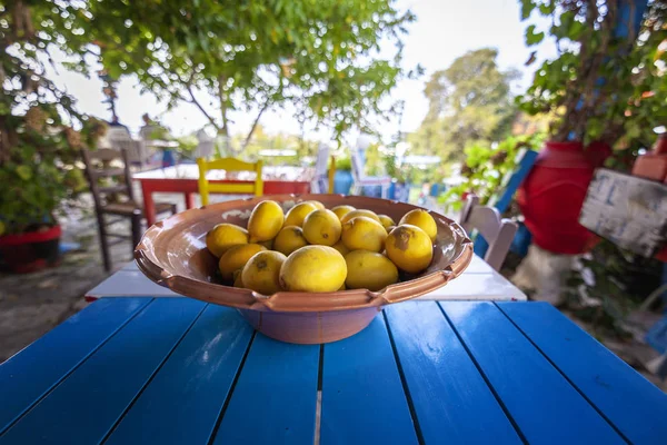 A large dish with bright yellow lemons on a bright blue table in a cafe