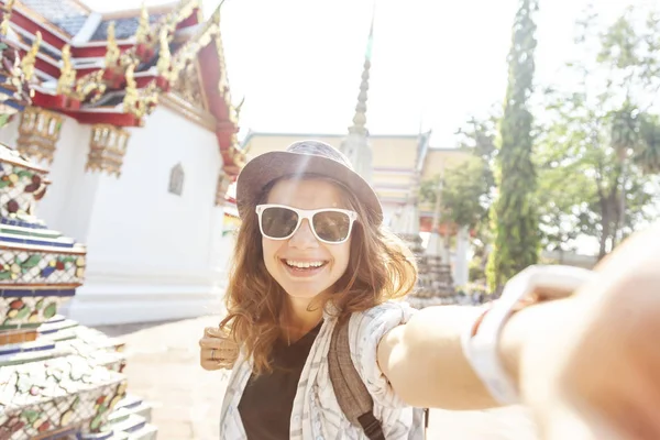 Young beautiful happy smiling european tourist woman in a hat and glasses at a buddhist temple in Bangkok traveling to southeast Asia