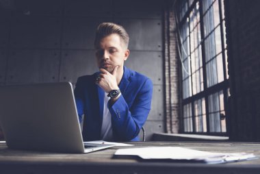 Mavi takım elbiseli adam genç çekici iş ofis dizüstü bilgisayar ve telefon, pazarlama ve iletişim yönetimi ile masada oturuyor