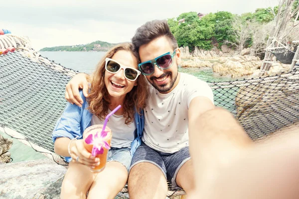 Young beautiful happy smiling funny couple man and woman best friends on a hammock on vacation makes selfie on  smartphone against the background of the sea