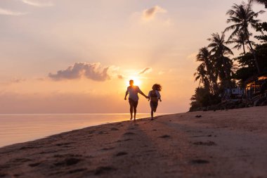 Aşık güzel mutlu genç çift sahilde kum boyunca deniz kıyısında bir balayı tatil tatil sırasında gün batımında çalışır