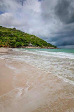 Tropikal bir plaj, karanlık fırtına bulutları, güzel etkileyici manzara, dalgalar ve beyaz kum, iklim değişikliği fırtınası