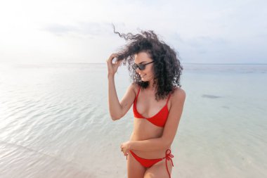 Güzel genç ince kadın güneş gözlüğü deniz arka planı siyah kıvırcık saçlı