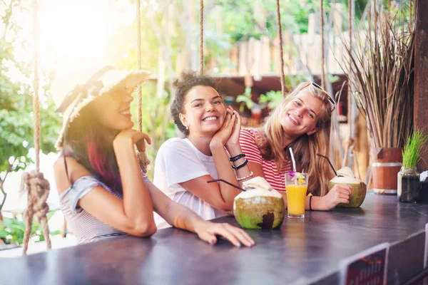 Trois jeunes belles petites amies minces boivent des cous et des noix de coco dans un élégant bar de plage — Photo
