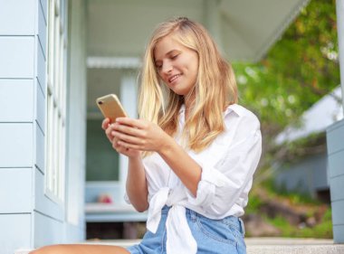 Güzel sarışın kız, yazlık Teras ev, onun elinde bir akıllı telefon ile güneş sahiptir