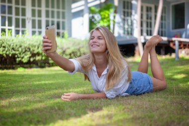 Güzel sarışın kız, onun elinde bir akıllı telefon ile bir yaz yeşil çim üzerinde güneşin sahiptir