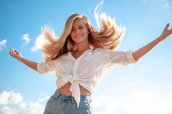 Hermosa joven rubia con el pelo que fluye y hoyuelos contra el cielo azul y el sol —  Fotos de Stock