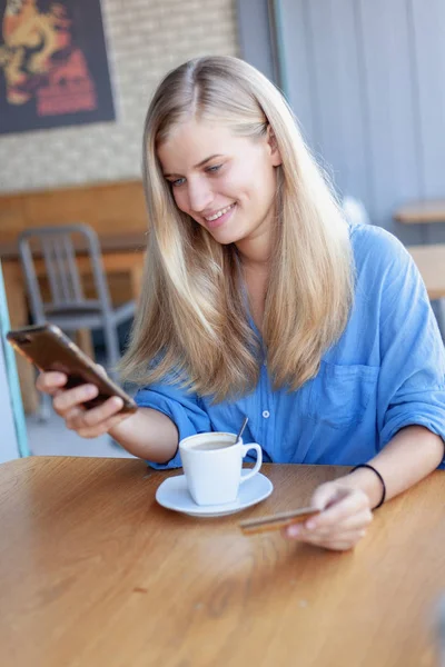 Beautiful young blonde girl cafe with a credit card in her hands — Stock Photo, Image