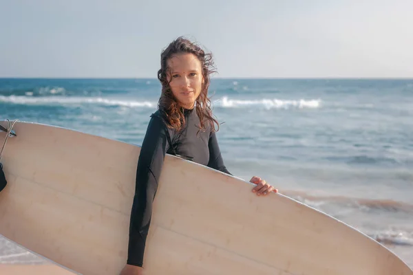 Hermosa joven en traje de baño caminando a lo largo de la orilla del océano con una tabla de surf en sus manos — Foto de Stock