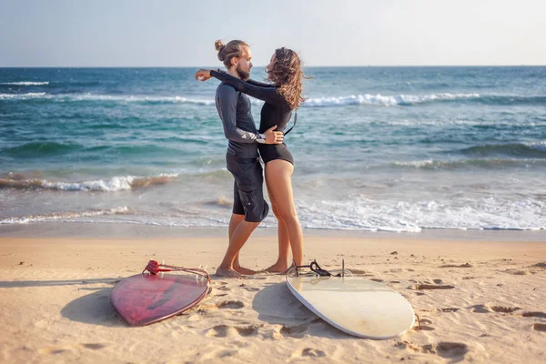 若い美しいカップルの友人は、砂の上にサーフボードで海に抱きついています,スポーツ — ストック写真