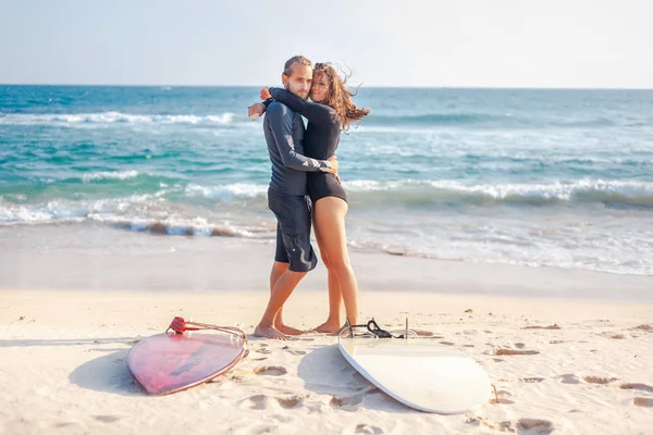 若い美しいカップルの友人は、砂の上にサーフボードで海に抱きついています,スポーツ — ストック写真