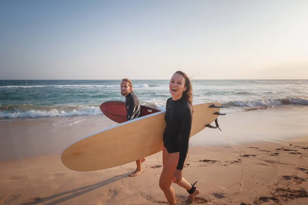 Jong stel blij glimlachende surfers aan de oceaan kust, sport actieve levensstijl vakantie reisconcept — Stockfoto