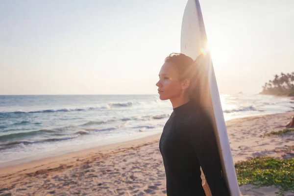 Jonge mooie vrouw met een surfplank op de oceaan met een surfplank in de stralen van t — Stockfoto