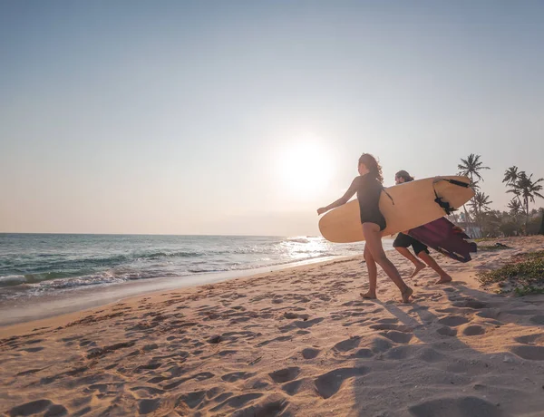 Jonge paar vrolijke glimlachende surfers lopen met surfplanken aan de oceaankust, sport actieve levensstijl — Stockfoto