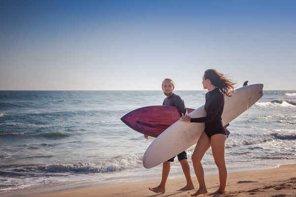 Young beautiful couple of friends on the ocean with surfboards in hands, sports, active lifestyle