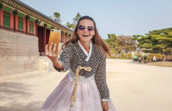 Glückliche europäische Touristin in koreanischer Tracht spaziert mit dem Handy durch die Paläste — Stockfoto