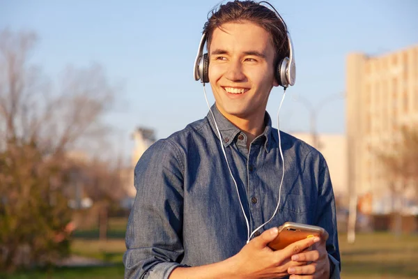 Lindo asiático adolescente chico escuchar música en auriculares en su teléfono, sonriendo disfrutando de la vista —  Fotos de Stock