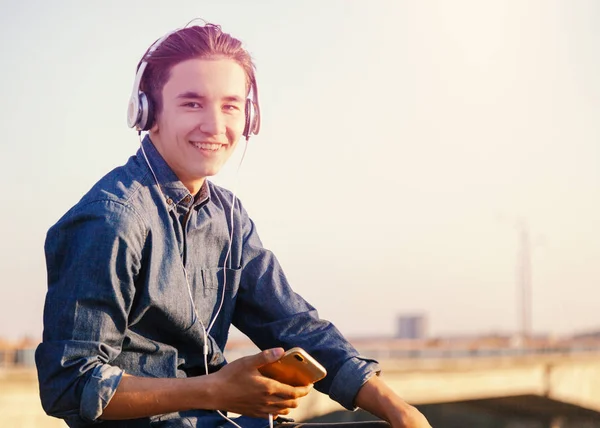 Lindo asiático adolescente chico escuchar música en auriculares en su teléfono, sonriendo disfrutando de la vista —  Fotos de Stock