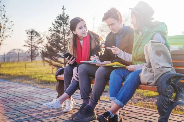 Groupe d'adolescents asiatiques écoliers assis sur un banc dans le parc et préparant des examens — Photo