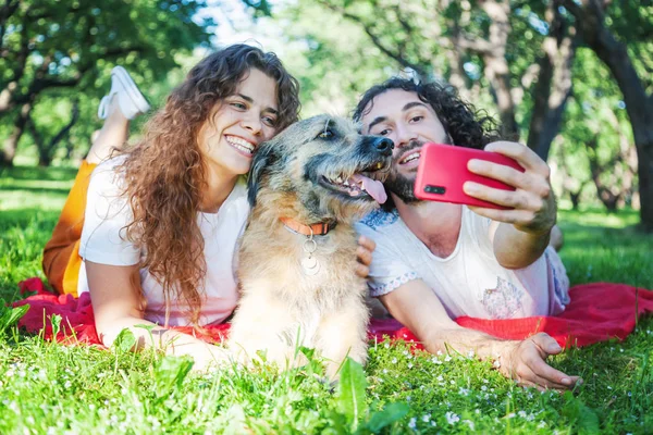 Young stylish couple playing with dog in park, making selfie pho — Stock Photo, Image