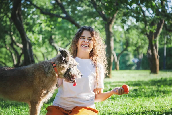 Ung lycklig charmig flicka leker med sin hund med en boll i — Stockfoto