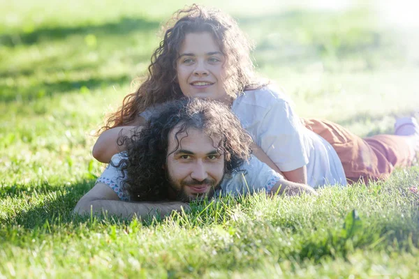 Glückliches junges lockiges Paar, das im Sommer auf dem grünen Gras liegt — Stockfoto