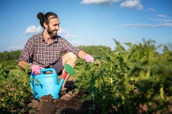 Young hipster male in gloves with a watering can caring for plan — Stock Photo, Image