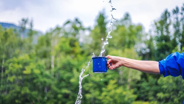 Blue camping mug with clear water, splashes on a forest backgrou — Stock Photo, Image
