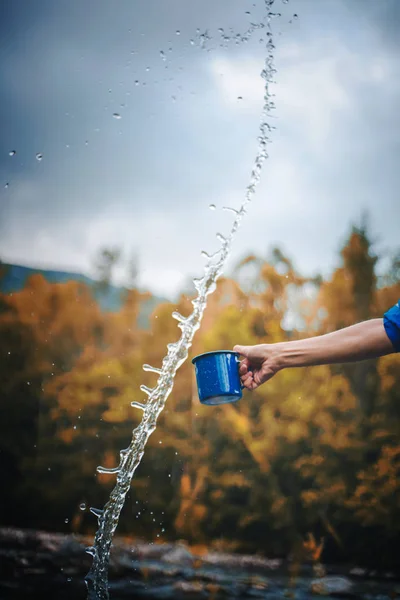 Taza de camping azul con agua clara, salpicaduras en un bosque backgrou — Foto de Stock