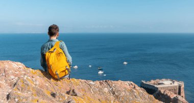 Sarı sırt çantalı genç bir gezgin okyanusa bakıyor.