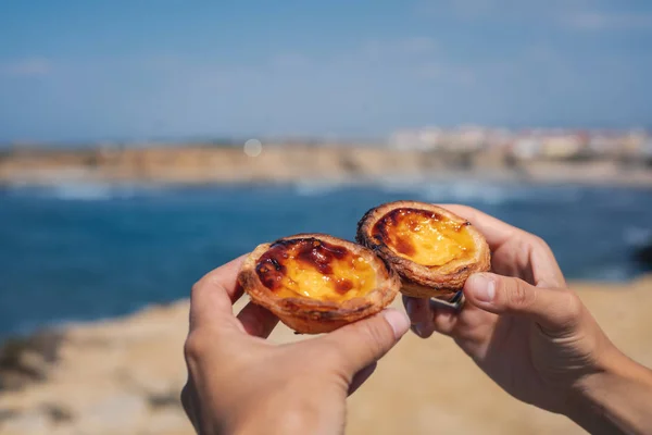 Pastel de nata in hand on a background of blue ocean, traditiona — Stock Photo, Image