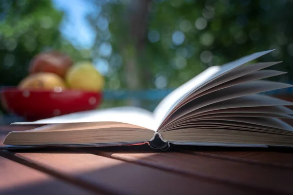 Prenota sul tavolo e chiudi la pagina con il piatto di frutta. Concetto di lettura estiva — Foto Stock