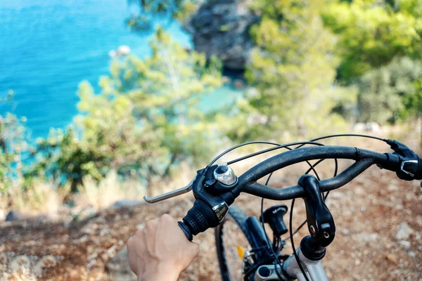 Eine weibliche Hand hält das Rad eines Fahrrads, schöne Landschaft mit dem Meer. Sommer-Radtour — Stockfoto