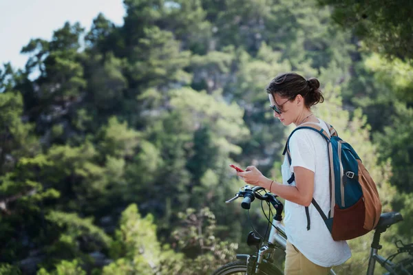 森の中で自転車を持っている女の子は スマートフォンの地図を見ています 夏休みと自転車での旅行 スポーツやアウトドア活動 — ストック写真