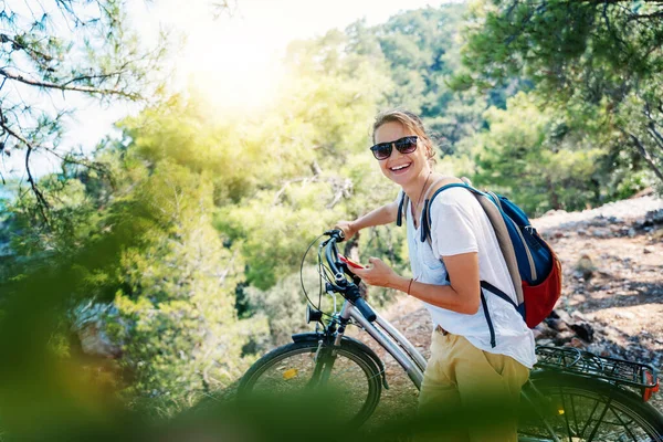 森の中で自転車を持っている女の子は スマートフォンの地図を見ています 夏休みと自転車での旅行 スポーツやアウトドア活動 — ストック写真
